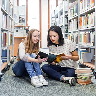 Jugendliche sitzen auf dem Boden in einer Bibliothek und lesen.