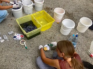 Jugendliche knien vor Plastikwannen und knoten Tücher.