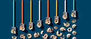 Acht gespitzte Buntstifte – türkis, rot, gelb und weiß – mit Spänen vom Anspitzer, angeordnet auf blauem Hintergrund.