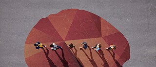 Draufsicht auf sieben Personen, die über ein großes geometrisches Muster in Rot- und Orangetönen auf grauem Untergrund gehen.