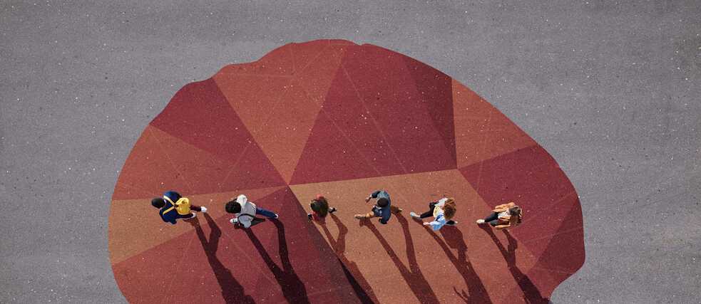 Draufsicht auf sieben Personen, die über ein großes geometrisches Muster in Rot- und Orangetönen auf grauem Untergrund gehen.