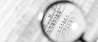 Nahaufnahme einer Lupe, die auf einen Abschnitt mit numerischen Daten gerichtet ist. Durch die Lupe sind Zahlen wie 2.68, 20.77 und +1.97 deutlich vergrößert sichtbar. Die Szene vermittelt den Eindruck einer genauen Analyse oder Prüfung von Zahlenmaterial.