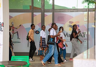 Youth participants at Kouman 2025 in Abidjan walk past a vibrant mural toward the entrance of MuCAT.