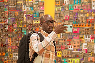 Teilnehmer beim Fotografieren auf der Kouman 2025 in Abidjan vor einer farbenfrohen Kulisse aus Miniaturfassaden, die die künstlerische und lebendige Atmosphäre der Veranstaltung widerspiegeln.