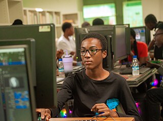 Teilnehmer arbeiten während der Kouman 2025 in Abidjan an Computerarbeitsplätzen in einem gut beleuchteten Raum, der mit Monitoren, Bücherregalen und diverser technischer Ausrüstung ausgestattet ist.