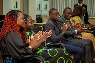 Engaged attendees at Kouman 2025, seated in a row and clapping enthusiastically, showcasing vibrant attire and active participation.