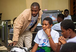 A group of Kouman workshop participants involved engaged in a learning session in front of a computer, with an instructor providing guidance. The students are focused on their screens, working with educational content in a classroom setting.