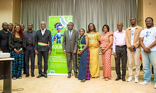 Group photo at Kouman 2025 in Yamoussoukro, featuring participants in traditional and formal attire standing before a vibrant Kouman banner promoting cultural connection through game design.