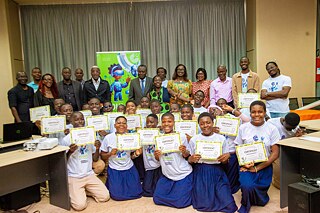 A group photo at Kouman 2025 event, featuring participants proudly holding certificates of participation in front of a colorful banner with the Kouman logo.