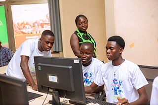 A group of participants in the Kouman workshop work together on a computer.