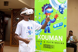 A Kouman workshop participant wearing a VR glasses in front of a Kouman banner. 