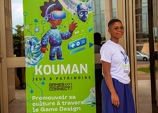 A Kouman workshop participant in front of a Kouman banner. 