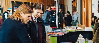 Young people and an advisor stand in front of stands with information brochures