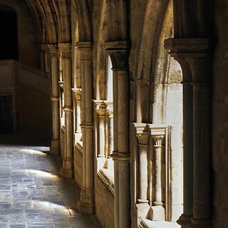 Steinbogen-Korridor mit Säulen, Sonnenlicht fällt durch die Bögen auf den Boden.