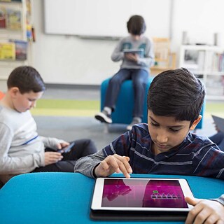 Ein Junge benützt in einer Bibliothek ein Tablet. Im Hintergrund weitere lesende Kinder mit Tablets.