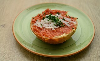A sliced white bread with raw red meat, onions and chives can be seen on a green plate.