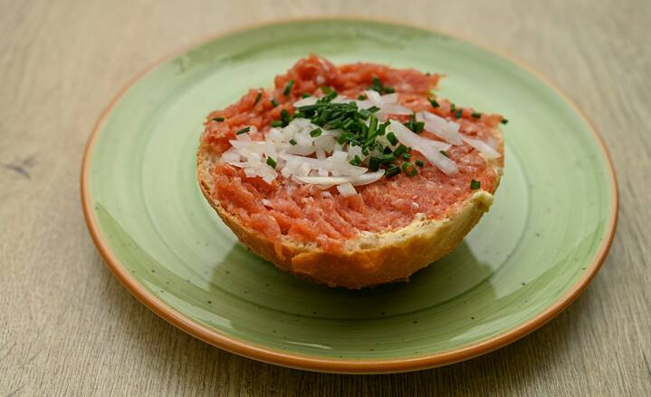 A sliced white bread with raw red meat, onions and chives can be seen on a green plate.