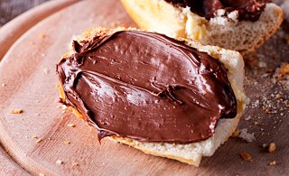 Ein Brot mit Nutellaaufstrich liegt auf einem Holzbrett.