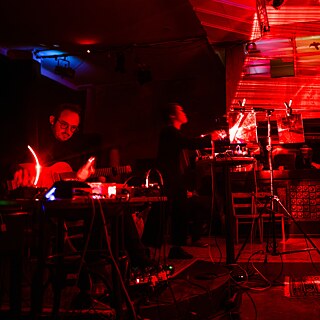 Ein männlich gelesener Mann mit einer Gitarre in einem Musikstudio.