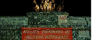 ein angestrahltes Brandenburger Tor mit Textbannern