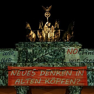 ein angestrahltes Brandenburger Tor mit Textbannern