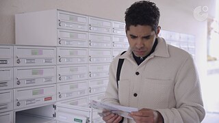 Eine Person steht vor einer Wand mit Briefkästen und hält mehrere Briefe in der Hand.