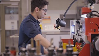 Eine Person arbeitet in einem Werkraum und bedient eine Maschine, umgeben von Werkzeugen und Geräten.