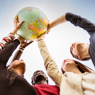 Jugendliche halten Weltkugel in die Luft.