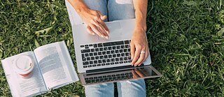 Eine Studentin lernt im Grünen – sie sitzt im Park im Gras und nutzt ihren Laptop.