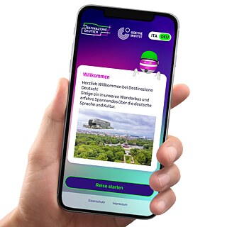 Ein Smartphone in einer Hand auf weißem Hintergrund; auf dem Bildschirm: Startseite des Projekts "Destinazione Deutsch"