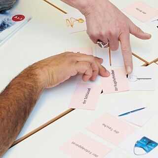 Kursteilnehmende machen eine Wortübung auf dem Tisch. Zu sehen sind Wortkarten und Lehrbücher.