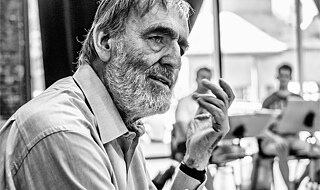 Ein dem Betrachter zugewandter Mann im Vordergrund, Musiker im Hintergrund.