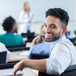 The image shows students in a German classroom attending a lecture. They are seated at desks, listening attentively to a presenter. The atmosphere is focused and welcoming, reflecting the academic environment of studying in Germany.