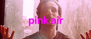 Person mit lockigem Haar, die in einem rosa gefärbten Licht sitzt. Über das Bild ist in großen, kräftigen, pinkfarbenen Buchstaben der Text „pink air“ geschrieben.
