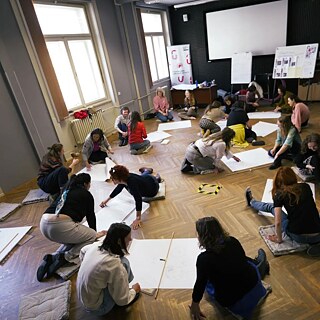  Inimesed istuvad põrandal ja joonistavad suurtele valgetele paberilehtedele.