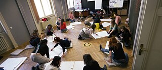  Inimesed istuvad põrandal ja joonistavad suurtele valgetele paberilehtedele.