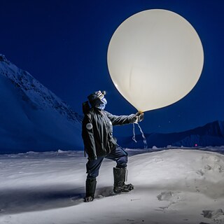 Key Visual Stars of Polar Night: Kvinne med en lysende værballon, i bakgrunnen et mørkt landskap av is og snø