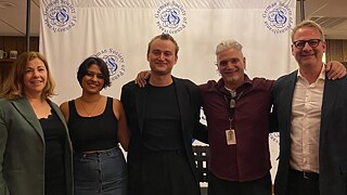 Sonali Beher and Iven Yorick Fenker stand alongside three others in front of a banner featuring the logo of the German Society of Pennsylvania.