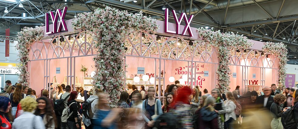 Zahlreiche Menschen passieren den zartrosanen Stand von LYX auf der Leipziger Buchmesse 2025.