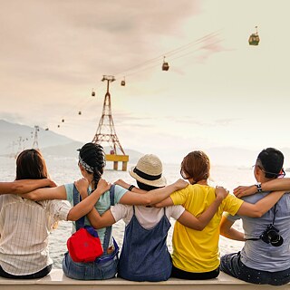 Jugendliche sitzen Arm in Arm und blicken auf eine Seilbahn.
