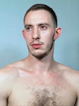 Portrait von Martin Talaga vor hellblauem Hintergrund, er posiert oberkörperfrei und schaut nach links aus dem Bild heraus.