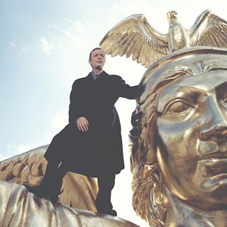 En mand med englevinger står på en tagkant og ser trist ud.