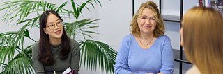 Drei Frauen im Gespräch. Zwei sind von vorne zu sehen und eine seitlich. Die Atmosphäre ist freundlich, interessiert. 