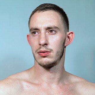 Portrait von Martin Talaga vor hellblauem Hintergrund, er posiert oberkörperfrei und schaut nach links aus dem Bild heraus.