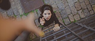 Eine Frau streckt ihre Hand nach oben aus, von oben ist eine weitere Hand zu sehen.