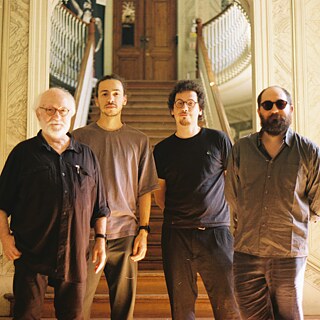 Das Foto zeigt das Streichquartett HEDERA 4TET. Die Musiker blicken alle in die Kamera und stehen nebeneinander. Im Hintergrund ist eine Treppe.