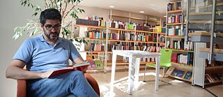 Ein Mann sitzt in einem roten Sessel in einer Bibliothek und liest.