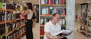 Zwei Personen in einer Bibliothek: Eine Frau steht und blättert durch Bücher in Bücherregalen, ein Mann sitzt davor und liest. 