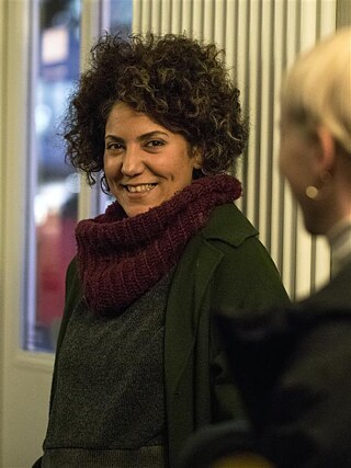 Narges Kalhor sonríe amablemente, llevando una bufanda color vino y un abrigo verde.