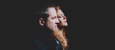 Un hombre y una mujer de perfil sobre un fondo negro – ambos con los ojos cerrados, en una actitud reflexiva y serena.